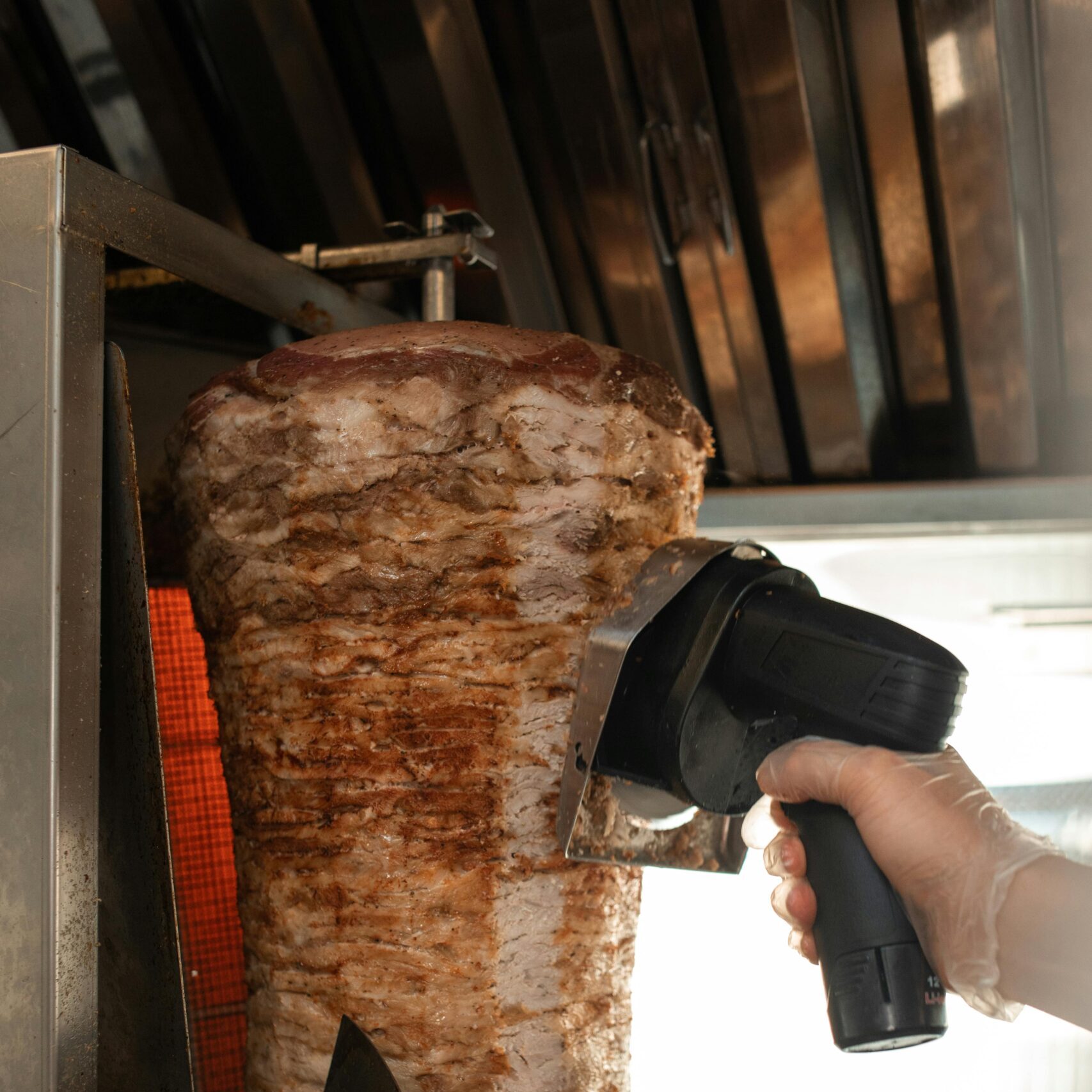 Close-up view of shawarma being sliced with professional equipment in a kitchen.